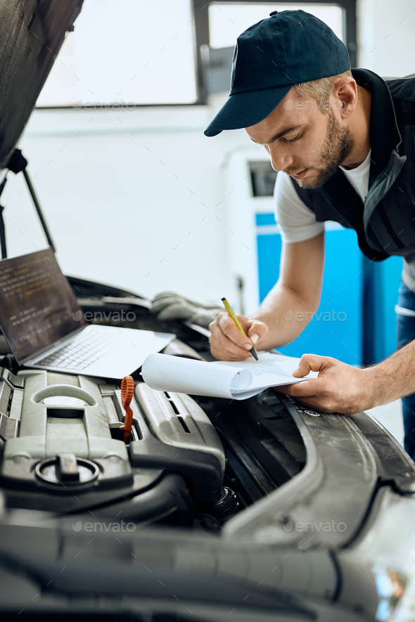 Auto mechanic writing notes while running car diagnostic and examining